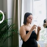 Mulher grava uma avaliação de produto em ambiente interno, usando câmera e iluminação circular.