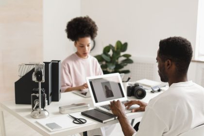 Dois profissionais colaboram em um escritório moderno, usando laptops ao lado de equipamentos de câmera.